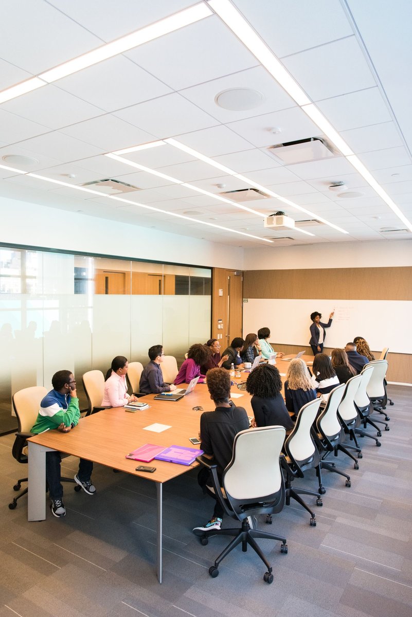 Large conference room with colleagues seated at a long table while a presenter writes on a whiteboard