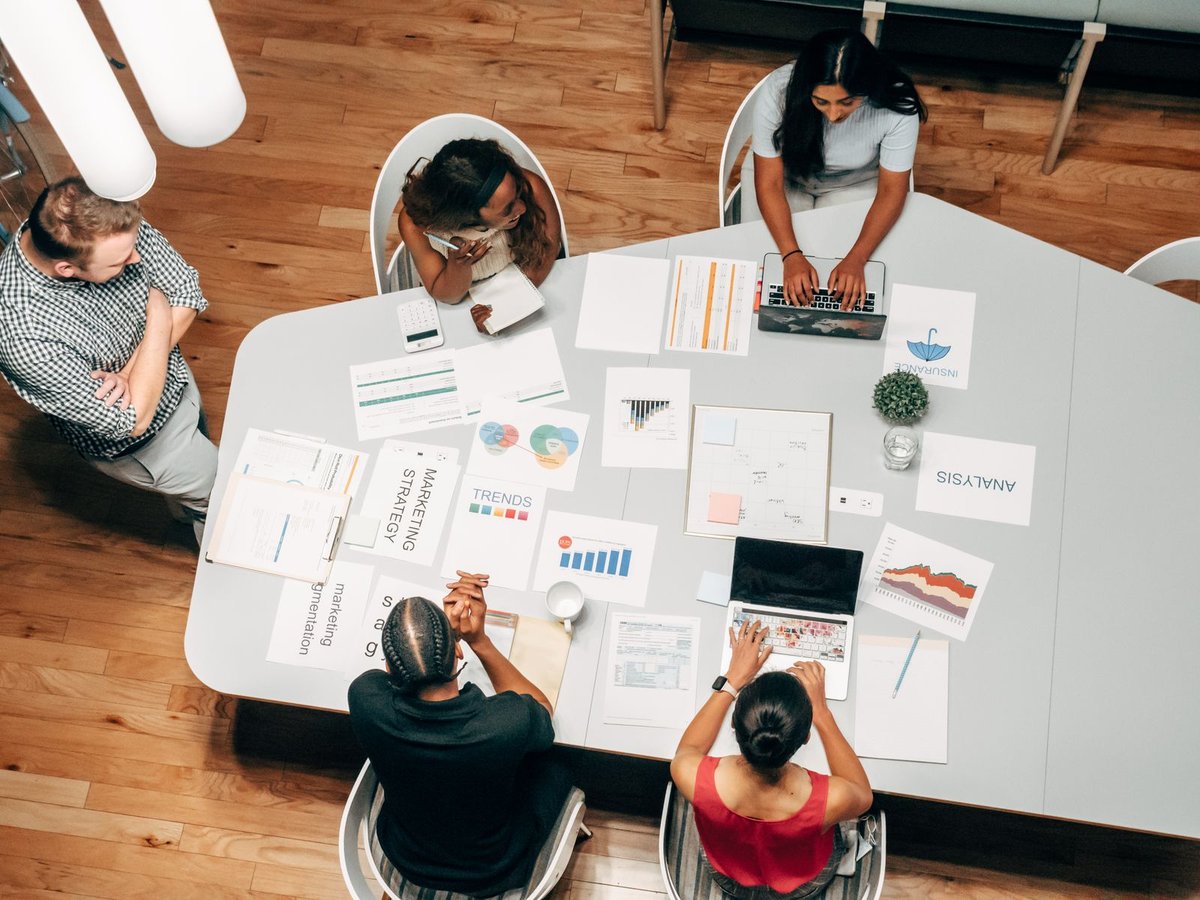 Overhead view of five colleagues around a meeting table with marketing strategy charts and laptops